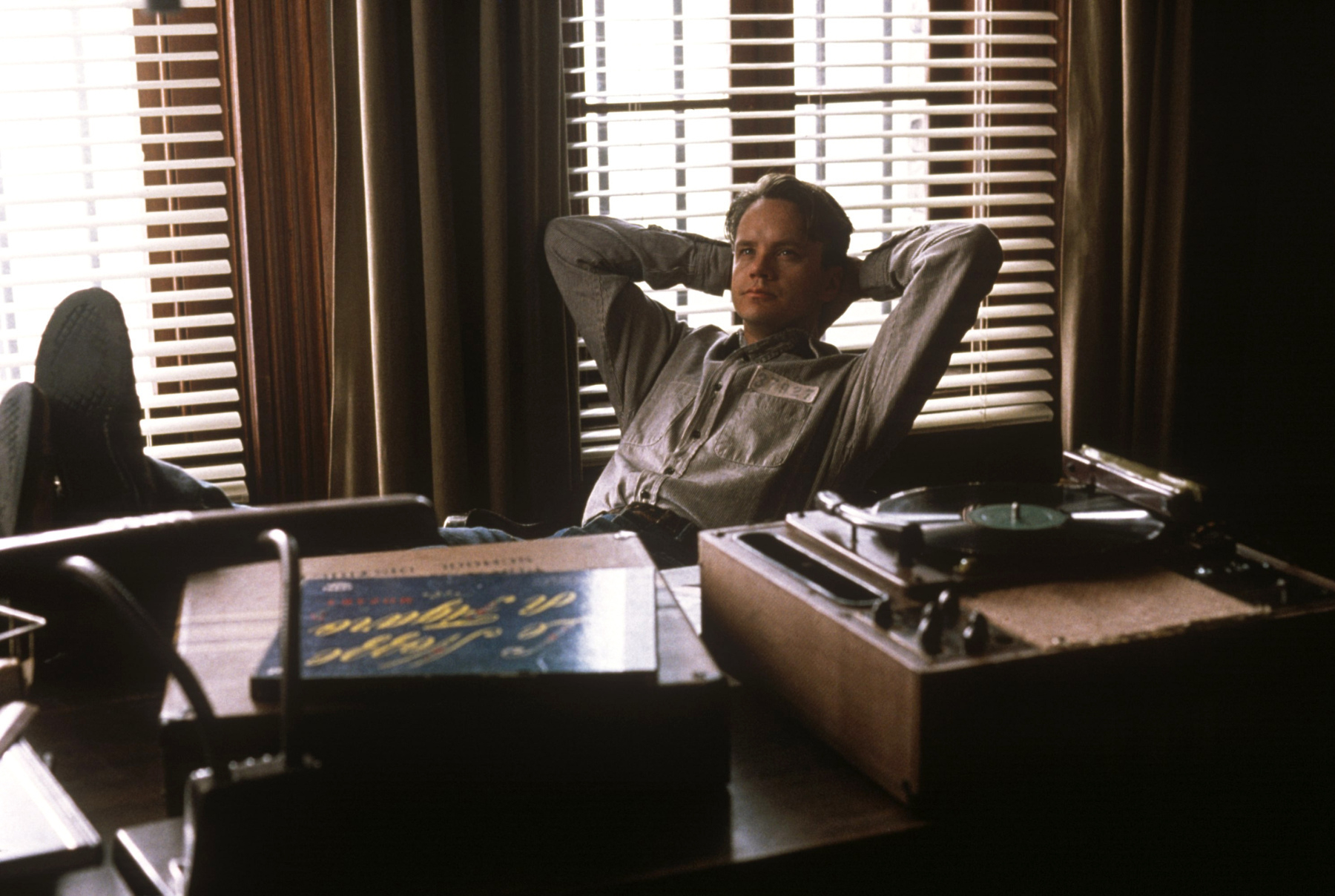 Andy sits on a desk with his feet up behind a record player.  