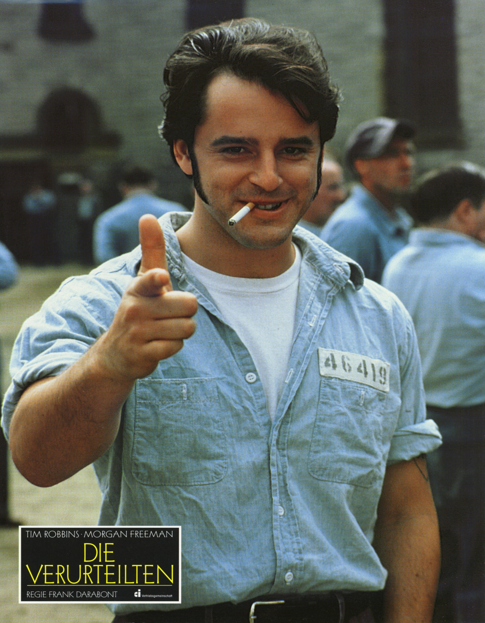 Young man in prison cloths with a cigarette in mouth pointing at the camera. 