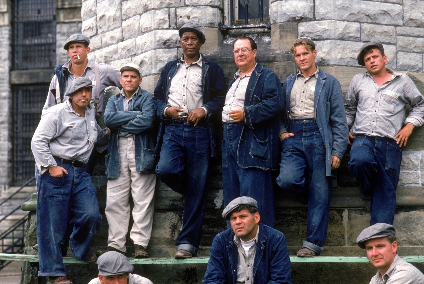 Movie still, The Shawshank Redemption: men in prison clothes leaning against a stone wall looking on. 