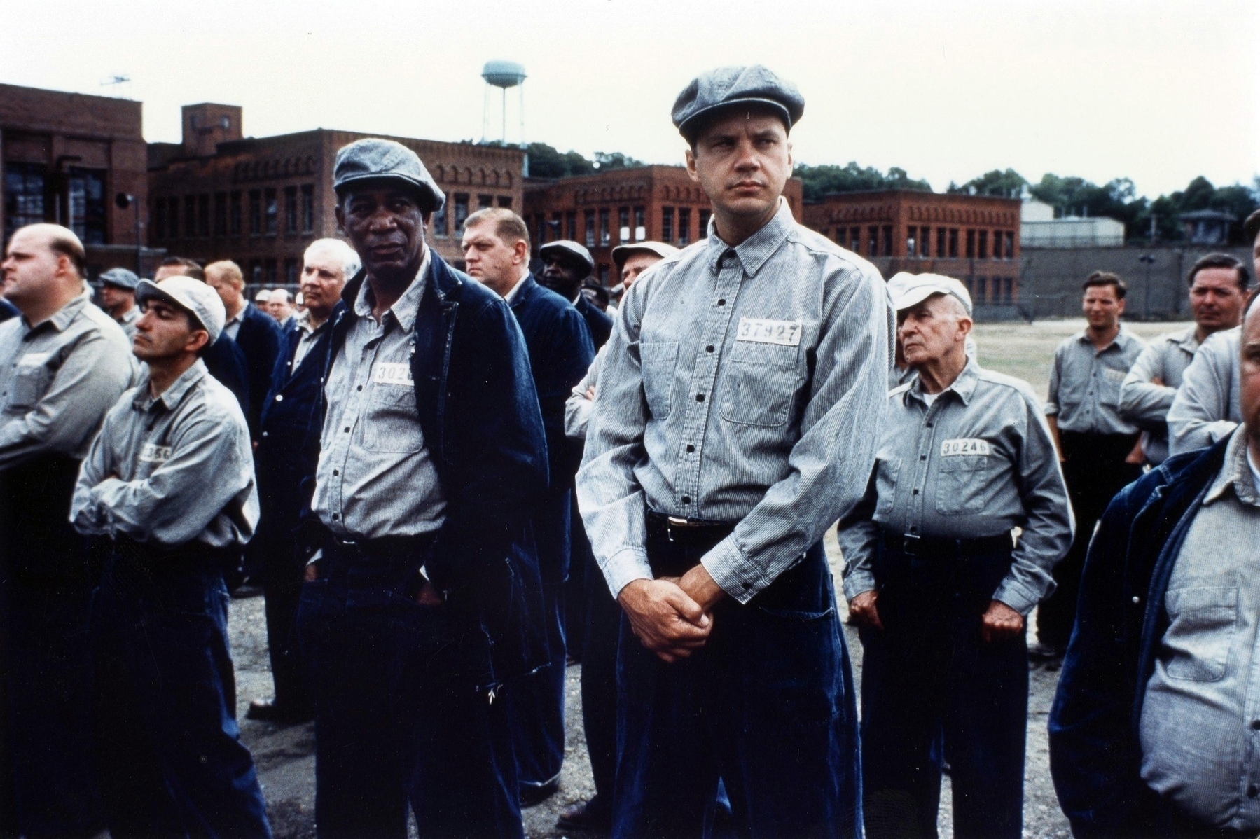 Movie still, The Shawshank Redemption: Two men stand next to each other in a prison yard wearing prison clothes. 