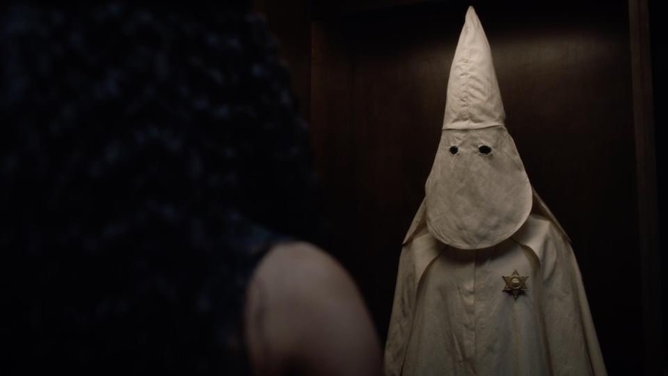 over the shoulder shot of a KKK uniform in a closet