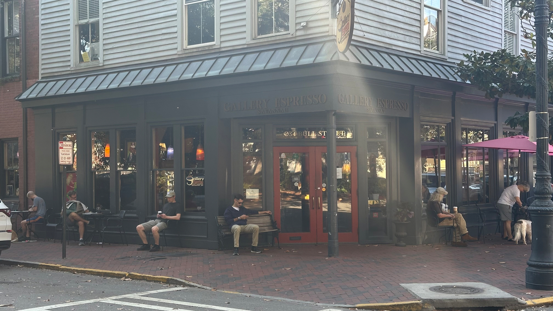 Exterior shot of coffee shop building. There are people lining the outside, sitting, reading 
