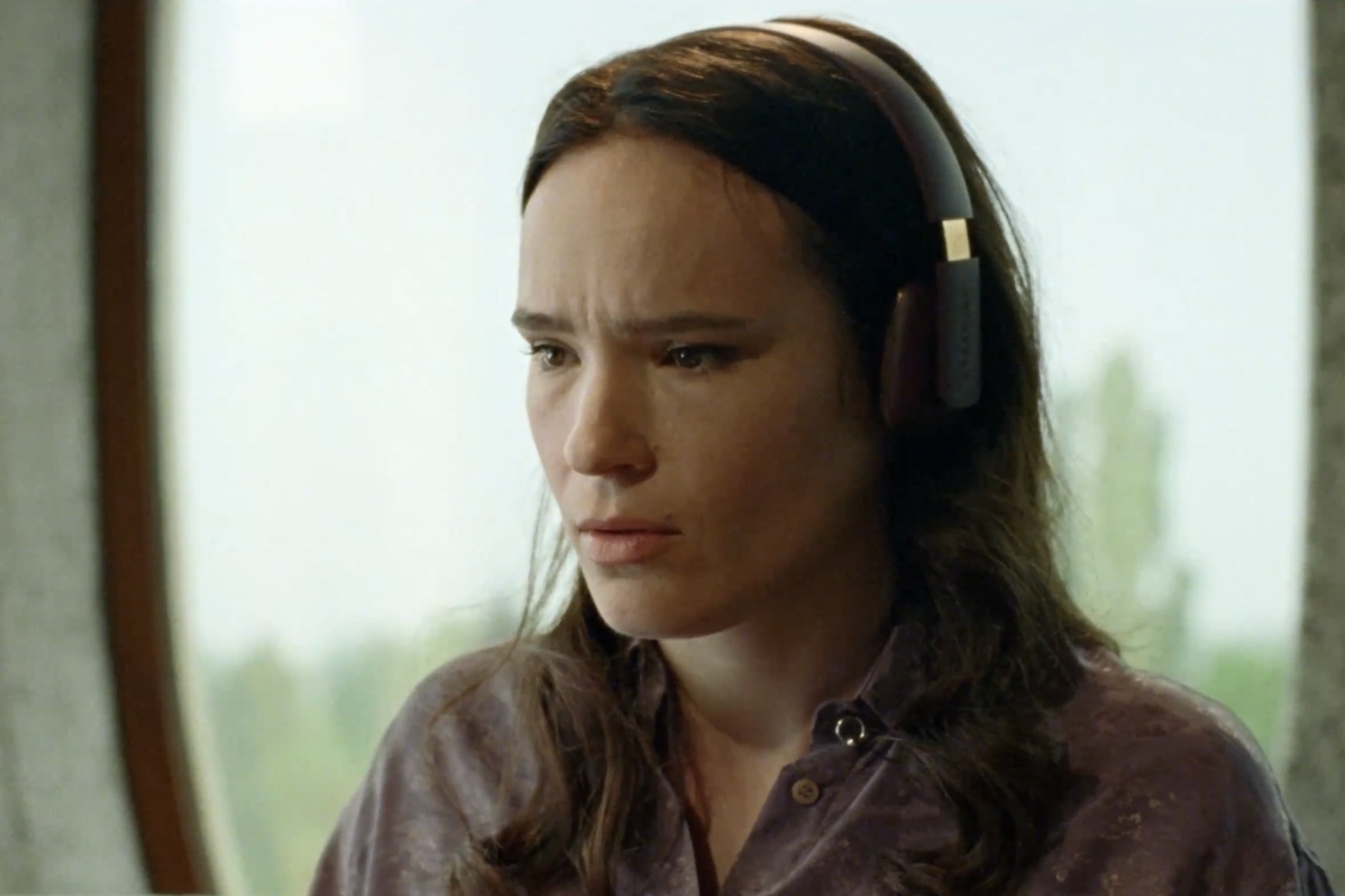 A woman with long brown hair and headphones on with a concerning look. 