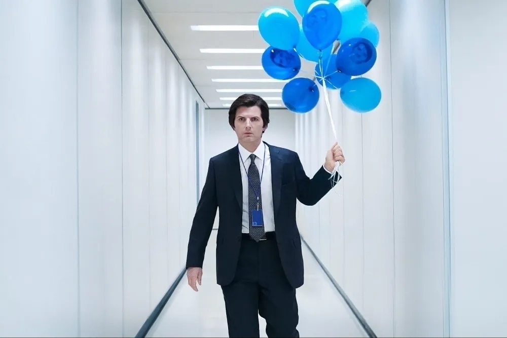 Man in a stark white hallway holding blue balloon balloons. 