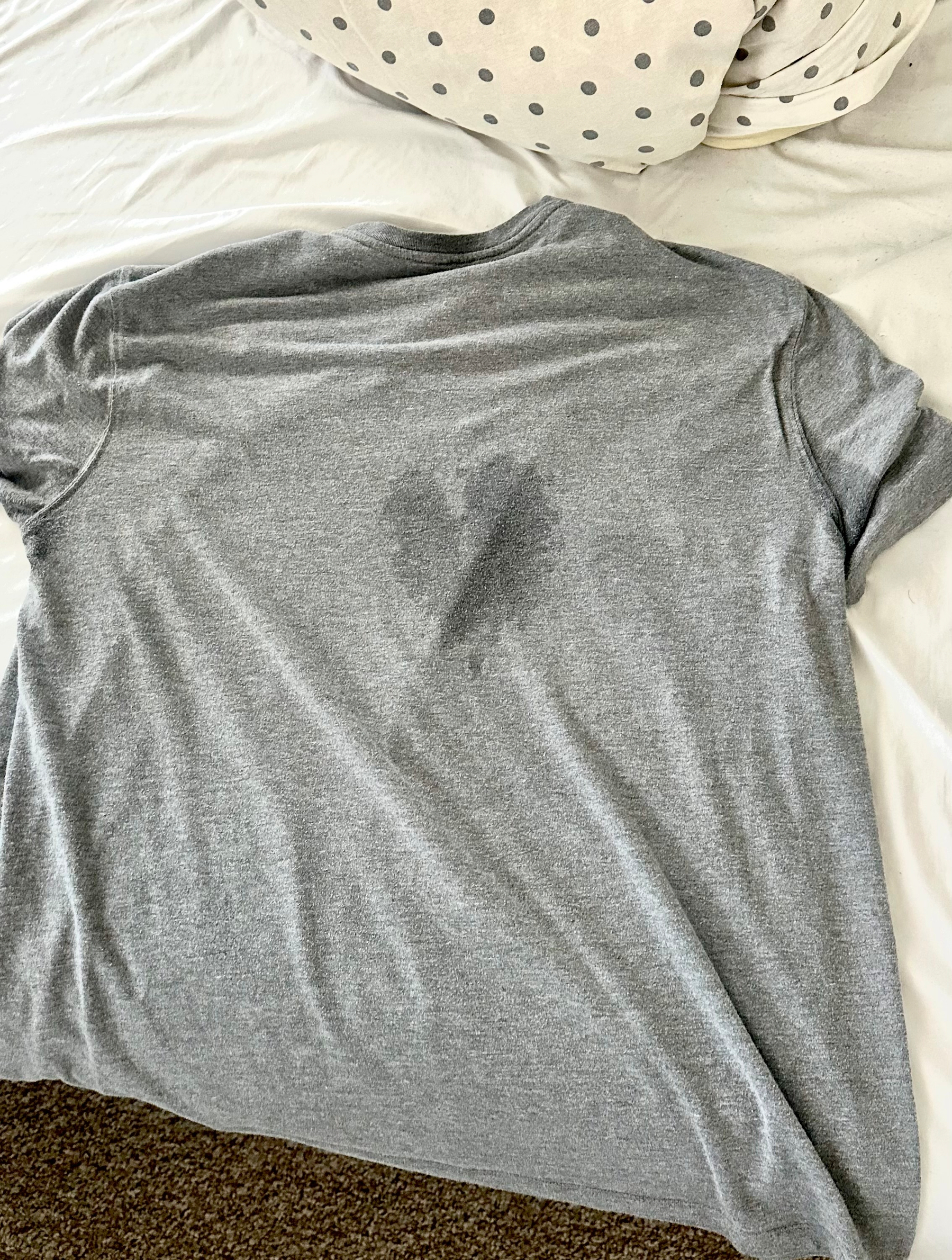 Grey t-shirt on the bed. There's a sweat stain on it in the shape of a heart. 