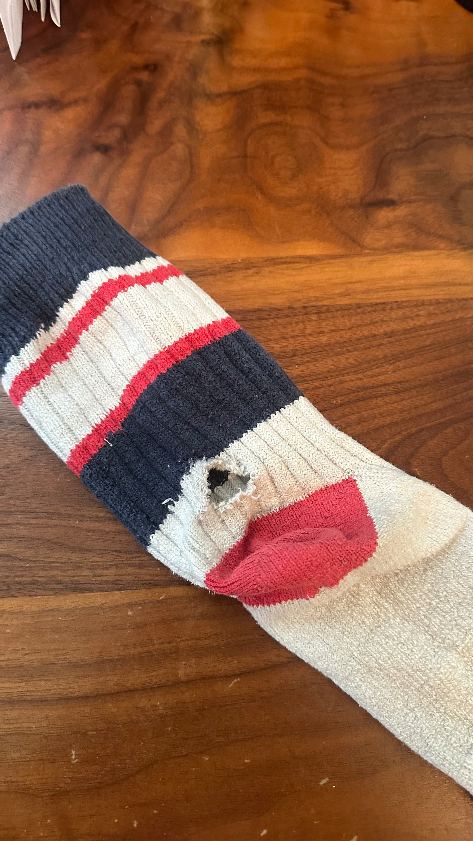 A crew sock with thick blue stripes and thinner red stripes. These a hole in the sock near and above the heel. Very sad. 