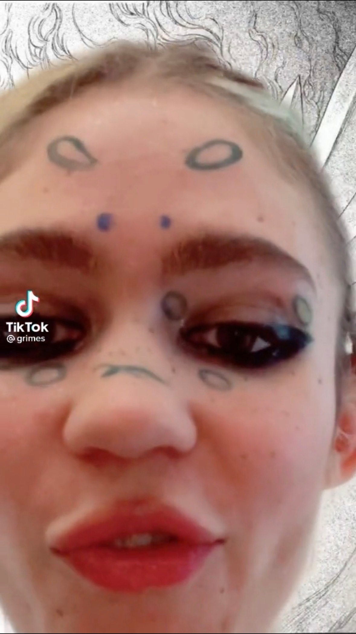 Screenshot of Grimes face close up. She's has rings pained on her face. 