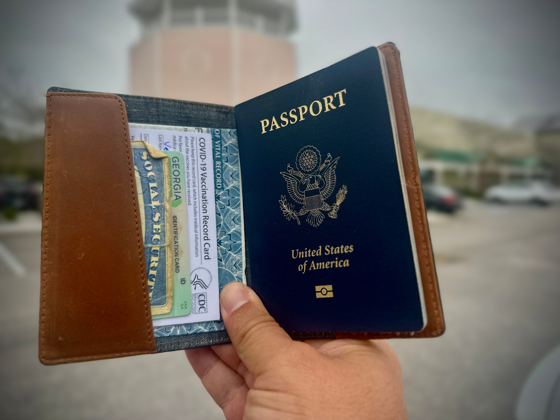 Photo of my hand holding an open passport wallet with a passport, ID, SSN card, COVID vaccination card, and birth certificate. 
