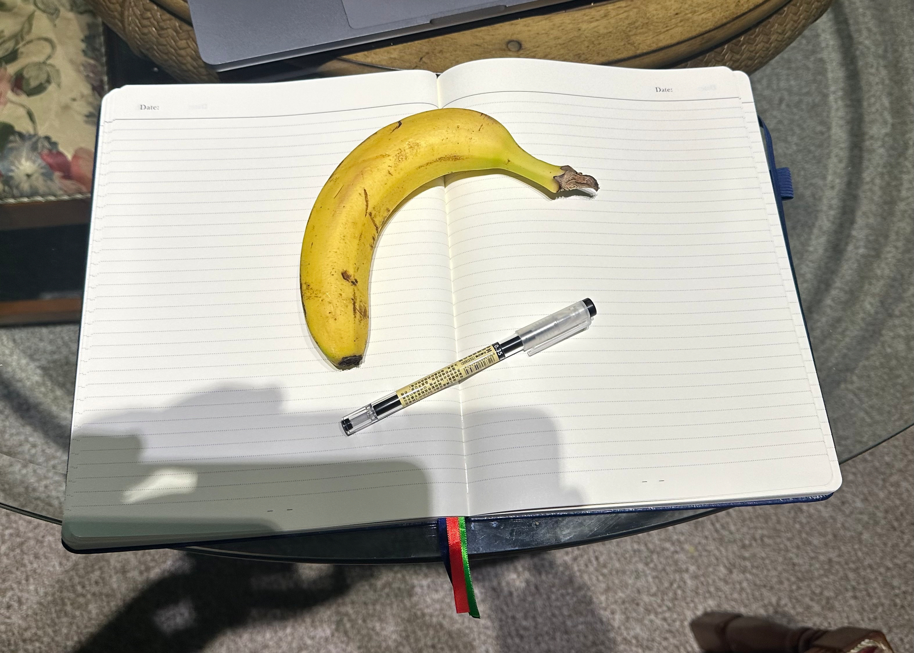 Open notebook with a pen and a banana on it for scale. The notebook is on a glass table top.