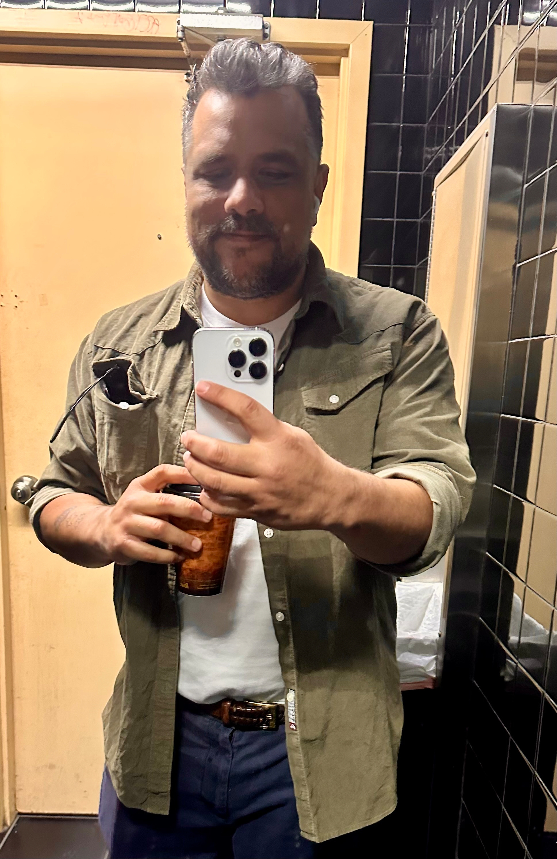 Bathroom selfie: I'm wearing an olive green button down with a brown weaved belt and blue chinos. I have a cup of coffee in my hand. 