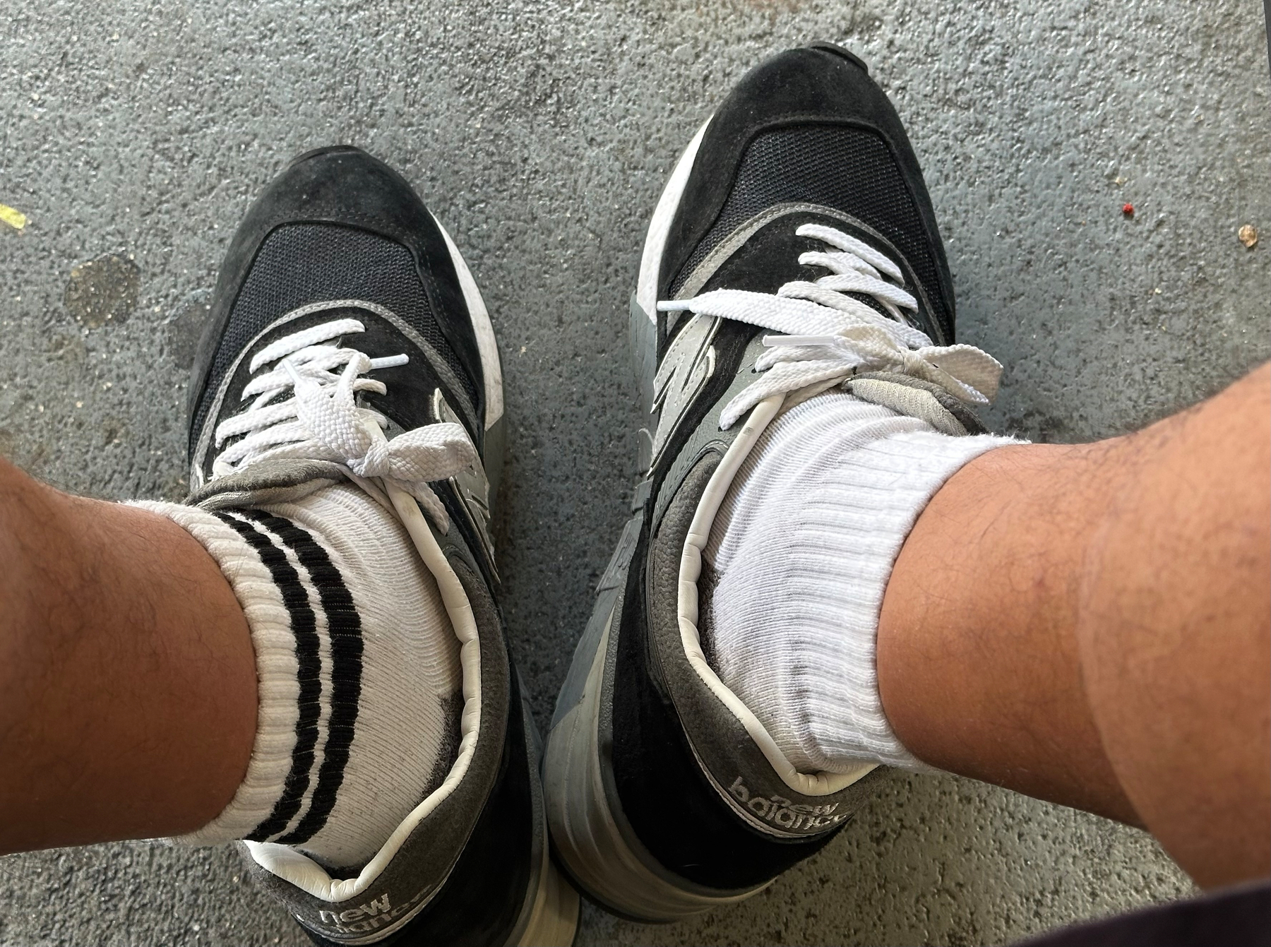 Photo of my shoes and lower legs on a concrete floor. I'm wearing one white and blue striped sock and one plain white sock. I'm wearing blue new balance sneakers. 