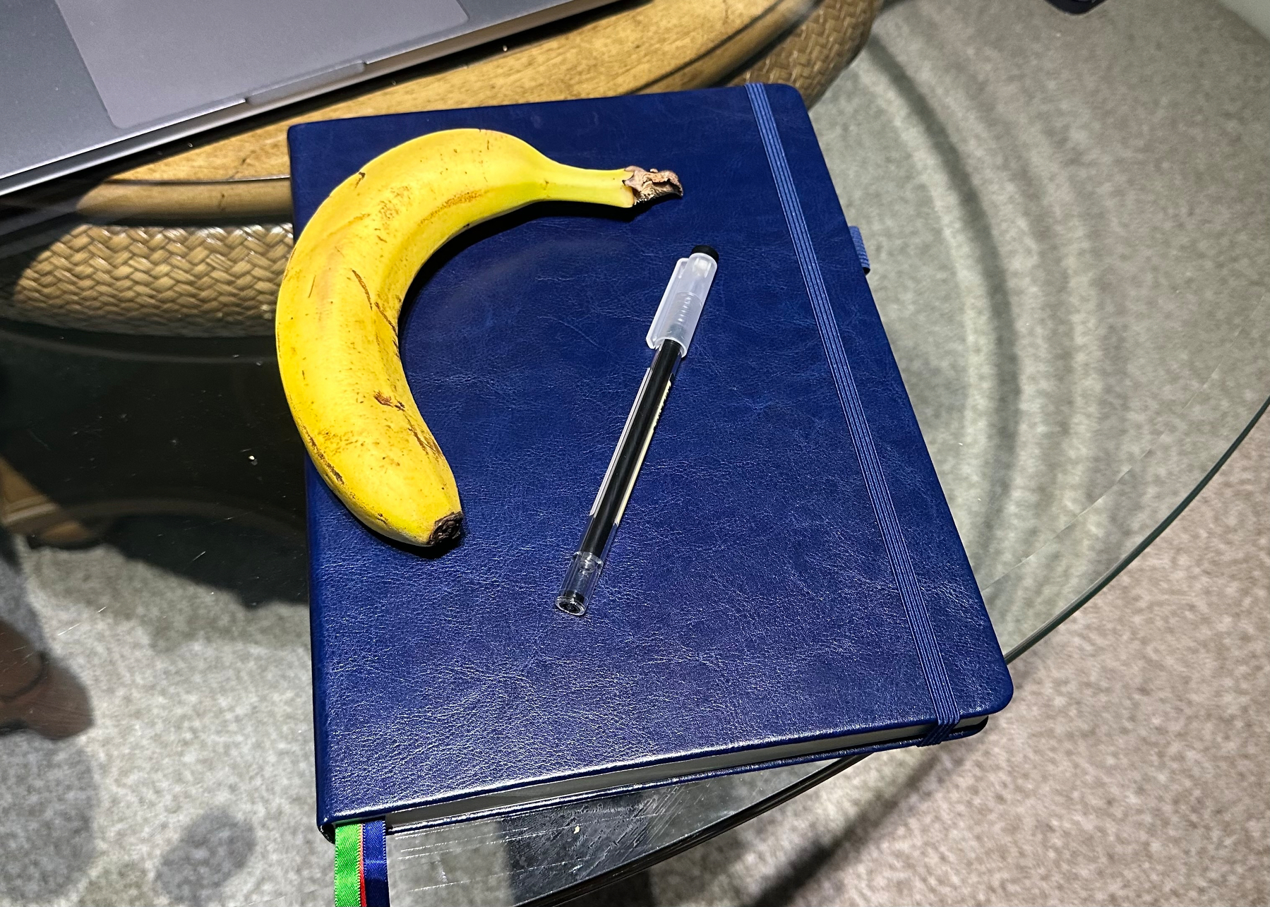 Blue notebook with a pen and a banana on it for scale. The notebook is on a glass table top.