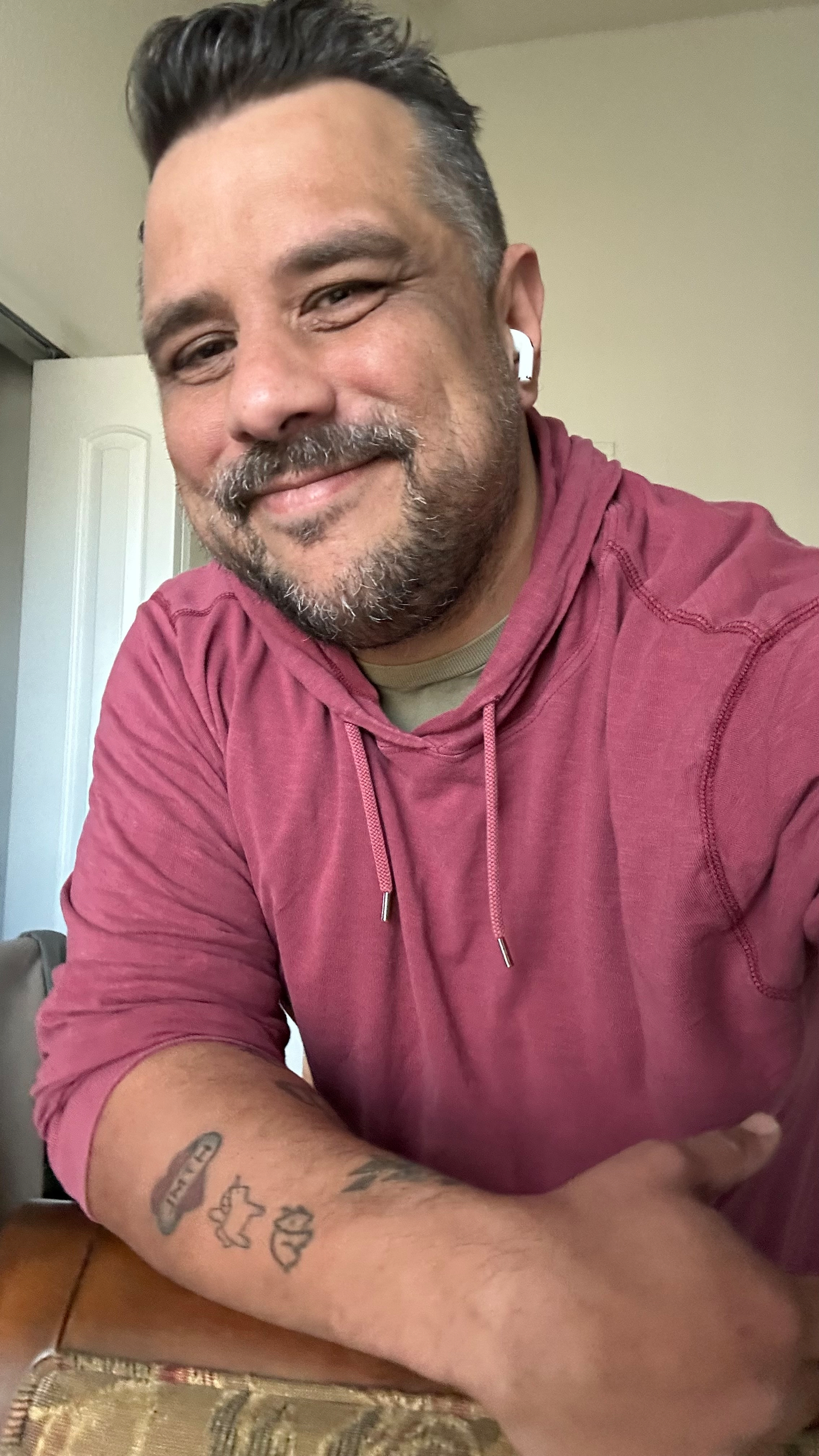 Me in a red hoodie shirt with a green undershirt, smiling. I have medium-short dark hair, earbuds on. 